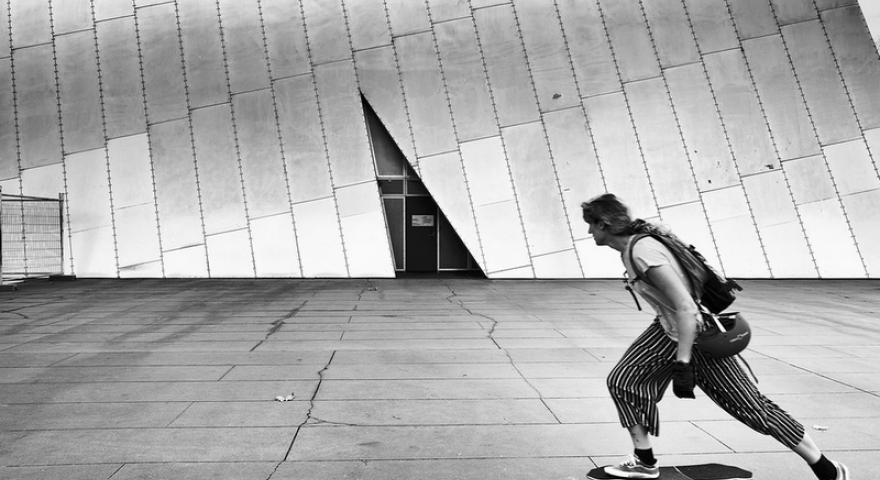A black and white image of a skater with a facade in the background that has a triangle shape reflected in the skaters posture.