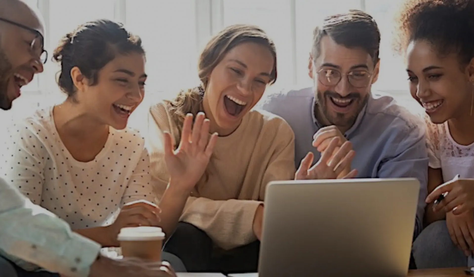 A group of people sit infront of a laptop smiling