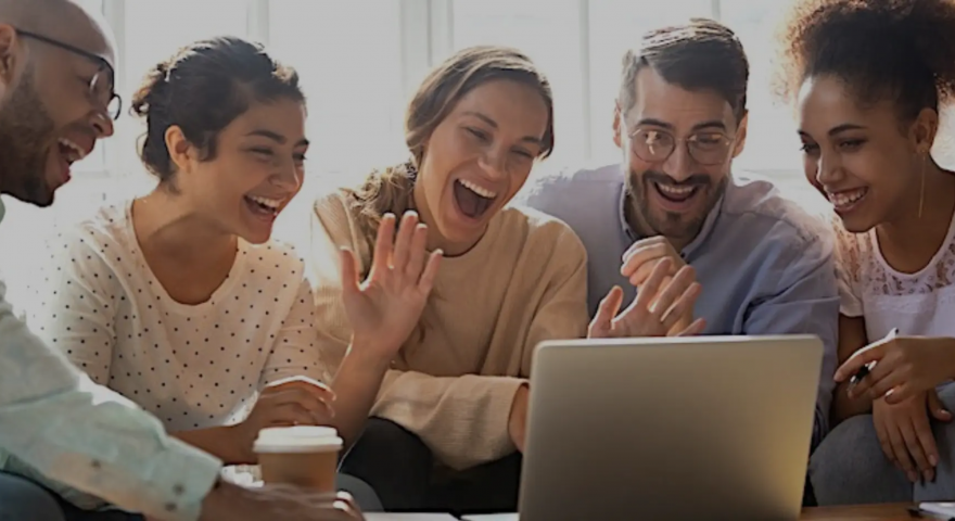 A group of people sit infront of a laptop smiling
